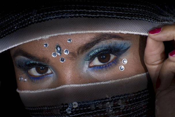 joven chica cara de cerca cubierto cara con lentejuelas tela mostrando sus ojos maquillaje
 - Foto, Imagen