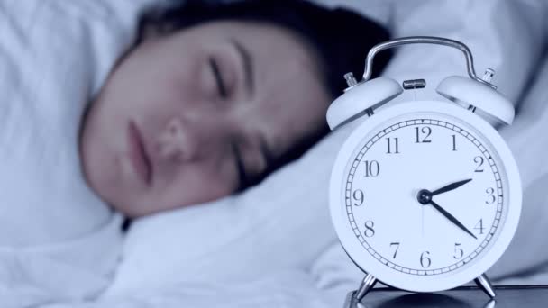Insomnia, anxiety, problems concepts. Attractive caucasian girl at night in bed looks at alarm clock and cannot fall asleep. Camera changes focus from clock to camera. Close-up - Filmati, video