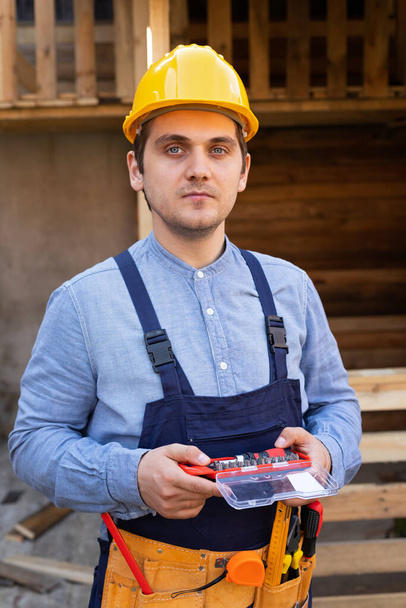 Portrait of a confident young workman wearing yellow helmet, blue uniform - DIY renovation concept - Foto, Imagen