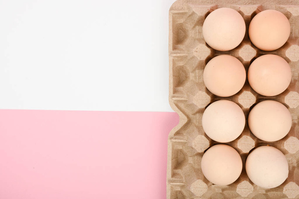 Egy tálca tojás, fehér és rózsaszín háttérrel. ökotálca herékkel. Minimalista trend, felülnézet. Tojásos tálca. Húsvét fogalma - Fotó, kép
