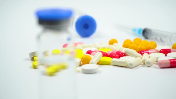 Gekleurde tabletten en pillen, medicijnfles en spuit op witte achtergrond. Medische voorbereidingen. 4k. Camera beweegt - Video