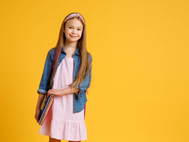 portrait of happy caucasian school girl with a book. beautiful positive girl with long red hair stand and hug her book, look at camera. she is preparing to school . isolated yellow background - Φωτογραφία, εικόνα