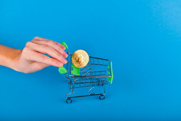 Bitcoin-Kaufkonzept. Bitcoin im Einkaufswagen, die Hand schiebt den Einkaufswagen, in dem sich Bitcoin befindet. auf dunkelblauem Hintergrund - Foto, Bild