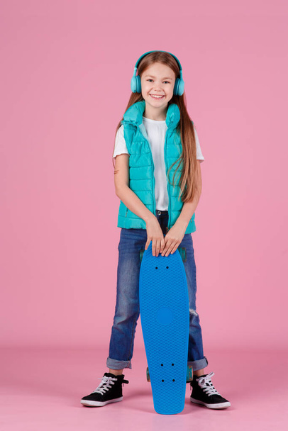 Beautiful little blonde kid girl 7-10 years old in jacket posing isolated on pastel pink background children portrait. Childhood lifestyle concept. Mock up copy space. Hold blue skateboard - Φωτογραφία, εικόνα