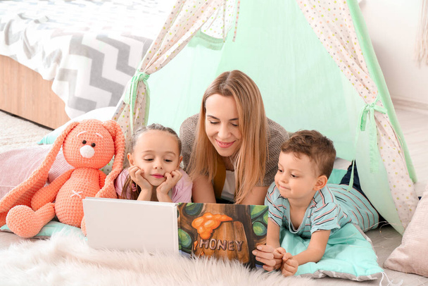 Nanny and cute little children reading book at home - Foto, imagen