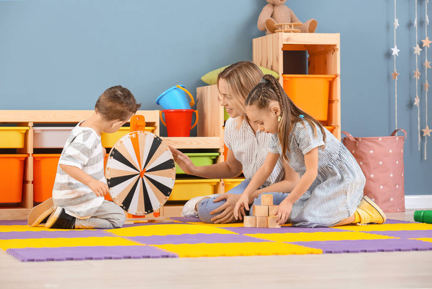 Niñera y niños pequeños y lindos jugando en casa
 - Foto, Imagen