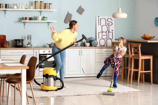 Jovem com sua filhinha se divertindo enquanto limpava a cozinha
 - Foto, Imagem