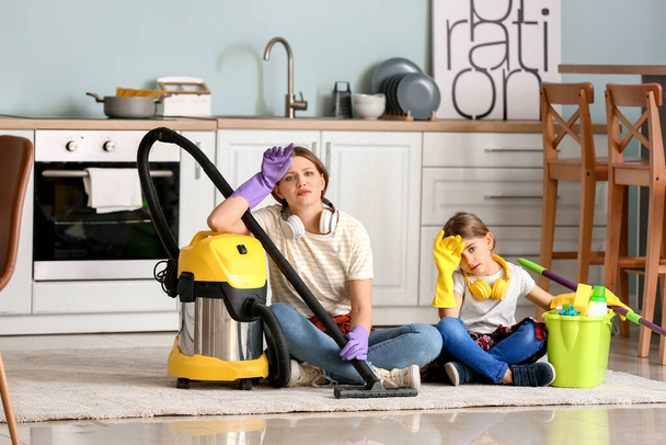 Κουρασμένη γυναίκα και η κορούλα της με ηλεκτρική σκούπα στην κουζίνα - Φωτογραφία, εικόνα