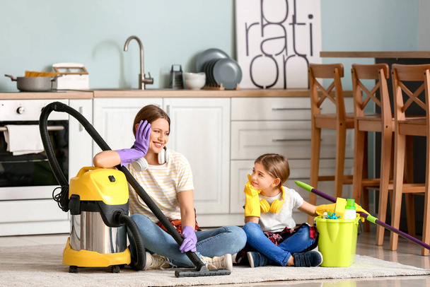 Young woman and her little daughter with vacuum cleaner in kitchen - Fotó, kép