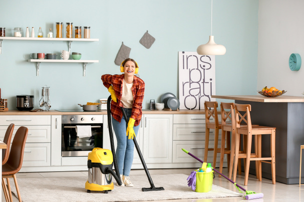 Young woman listening to music while hoovering floor in kitchen - Photo, image