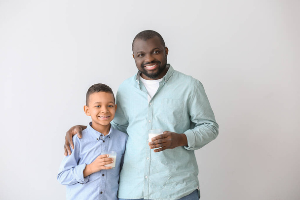 African-American man and his son with milk on light background - Φωτογραφία, εικόνα