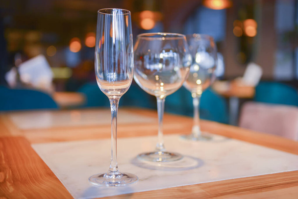 Transparent empty champagne and wine glasses on the rustic wooden table over blurred restaurant background. - Фото, изображение