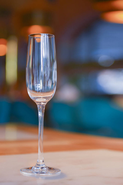 Transparent empty champagne glass on the rustic wooden table over blurred restaurant background. - Фото, изображение