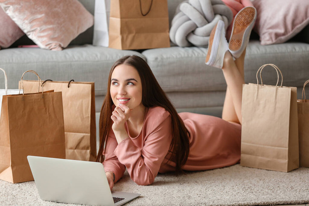 Junge Frau mit Laptop und Einkaufstasche zu Hause - Foto, Bild