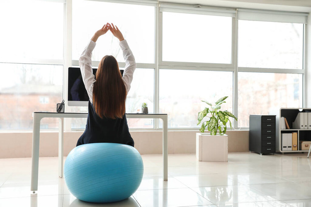 Деловая женщина, сидящая на фитнес-мяч во время работы в офисе
 - Фото, изображение