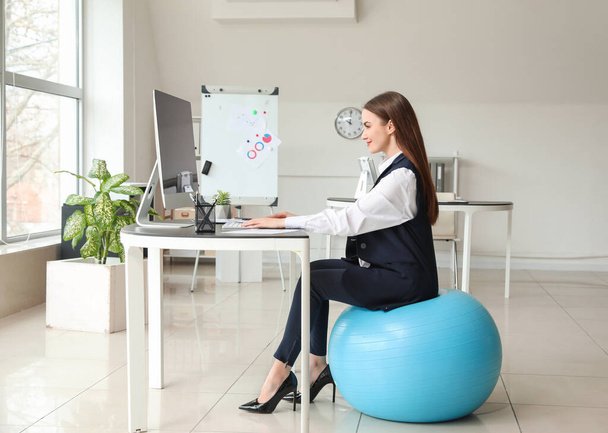 Businesswoman sitting on fitness ball while working in office - Foto, imagen