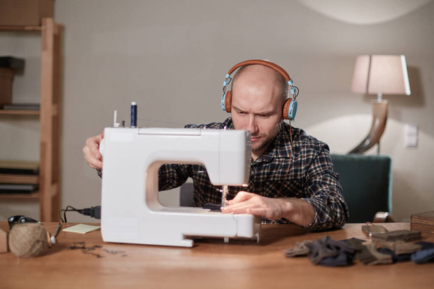 L'uomo ascolta musica e lavora con la macchina da cucire in uno studio tessile. Sarto fa papillon di tessuto di lana
. - Foto, immagini