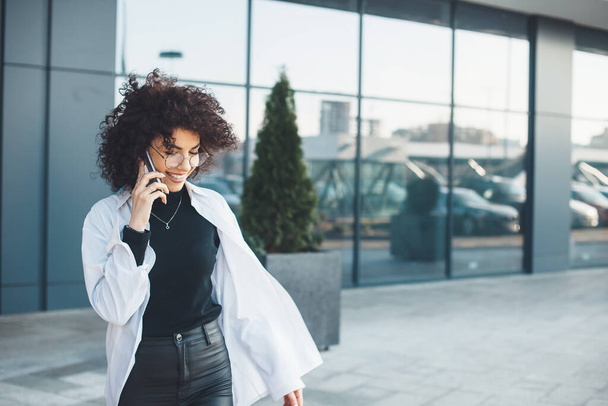 Caucasica dai capelli ricci donna d'affari caucasica che parla al telefono con un imprenditore fuori in camicia bianca
 - Foto, immagini