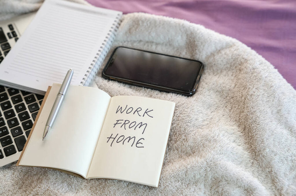 Work from home, text written on notepad. Computer laptop, cellphone and notepad on top of bed in the bedroom. - Fotografie, Obrázek
