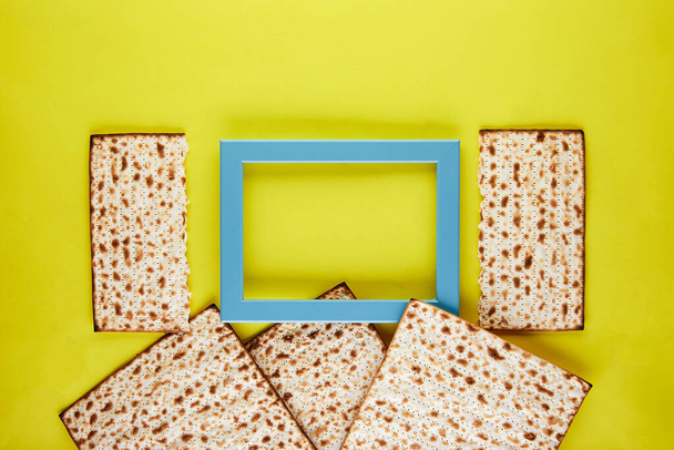Pesah celebration concept - jewish Passover holiday. Matzo background on a yellow background with a blue frame. View from above. Flat lay. Copy space. - Photo, Image