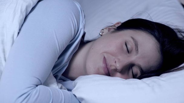 Dívka spí a usmívá se. Koncept sladkých snů. Mladá atraktivní běloška spí sama v posteli objímající polštář a zažívá pozitivní emoce. Detailní záběr - Fotografie, Obrázek