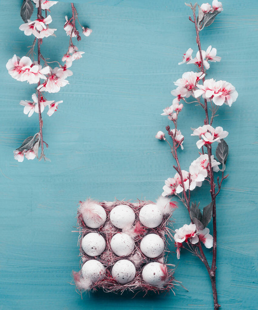 Beautiful Easter background. Spring blossom branches frame and egg-crate with Easter eggs at blue, top view with copy space for your design - 写真・画像