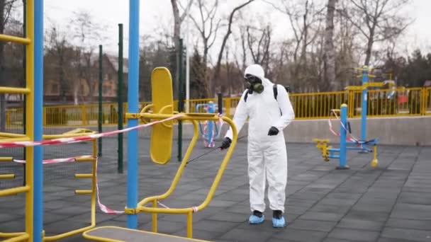 Hazmat worker disinfects sports ground surfaces from coronavirus covid-19 hazard with antibacterial sanitizer sprayer on quarantine. Man in protective suit cleans public athletic fitness equipment. - Metraje, vídeo