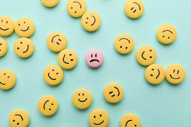 Eine rosa Pille mit gezeichnetem traurigem Gesicht unter Glücklichen auf farbigem Hintergrund - Foto, Bild