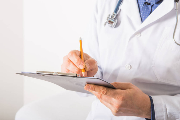 Doctor con estetoscopio escribiendo prescripción de RX en portapapeles sobre fondo blanco, primer plano. Servicio médico
 - Foto, Imagen