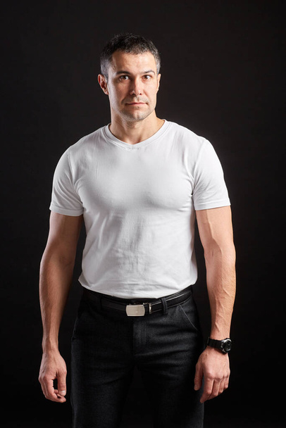 Beau sportif homme en blanc blanc t-shirt blanc debout sur fond de mur noir
 - Photo, image