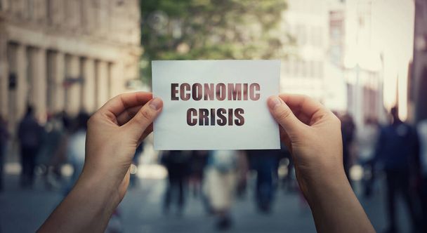 Руки держат бумажный лист с предупреждением о концепции глобального экономического кризиса на переполненном уличном фоне. Мировая рецессия, экономический коллапс из-за пандемии COVID-19. Символ финансового риска
. - Фото, изображение