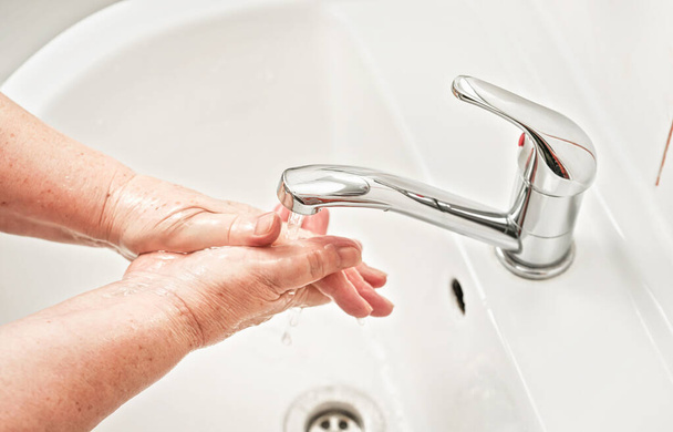Mujer mayor lavándose las manos con jabón bajo el grifo de agua del grifo. Puede utilizarse como concepto de ilustración de higiene durante el brote de coronavirus / covid 19 de ncov
 - Foto, Imagen