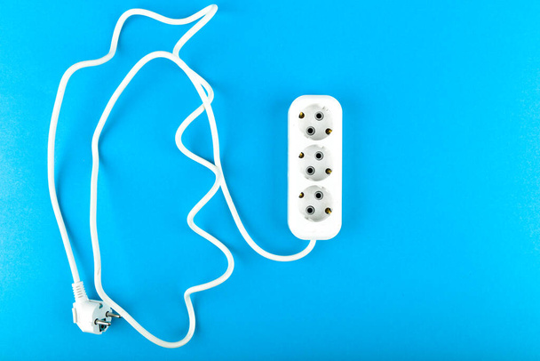 White socket with wire. View from above. on a blue background. White socket and extension cord. Extension cord for three outlets with a long spiral cord - Photo, Image