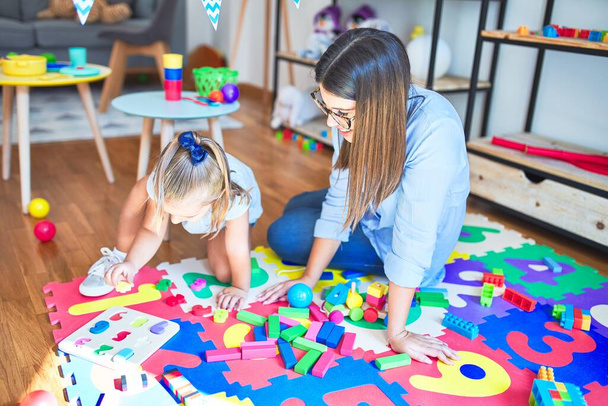 Καυκάσιο κορίτσι παίζει και μαθαίνει στο σχολείο με μια δασκάλα. Μητέρα και κόρη στο playroom γύρω από παιχνίδια που παίζουν με ογκόλιθους - Φωτογραφία, εικόνα