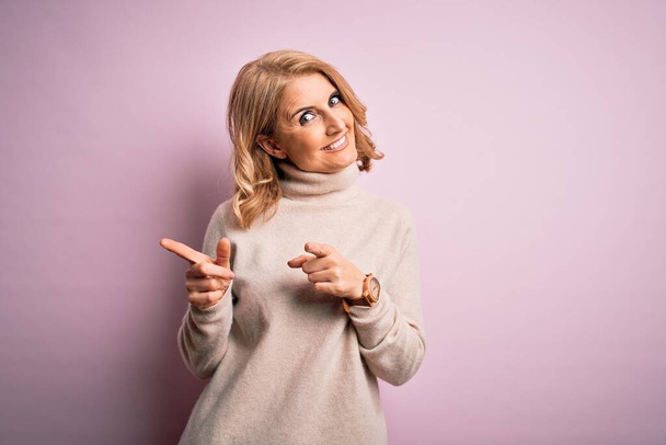 Μέση ηλικία όμορφη ξανθιά γυναίκα φορώντας casual ζιβάγκο πουλόβερ πάνω από ροζ φόντο δείχνοντας τα δάχτυλα στην κάμερα με χαρούμενο και αστείο πρόσωπο. Καλή ενέργεια και δονήσεις. - Φωτογραφία, εικόνα