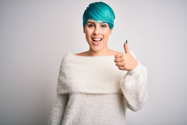 Young beautiful woman with blue fashion hair wearing casual sweater over white background doing happy thumbs up gesture with hand. Approving expression looking at the camera showing success. - Foto, Imagen
