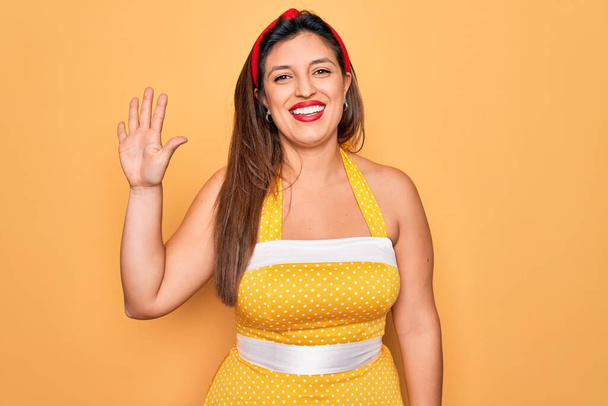Junge hispanische Pin-up-Frau trägt Mode sexy 50er Jahre Stil auf gelbem Hintergrund zeigt und zeigt mit Fingern Nummer fünf, während sie selbstbewusst und glücklich lächelt. - Foto, Bild