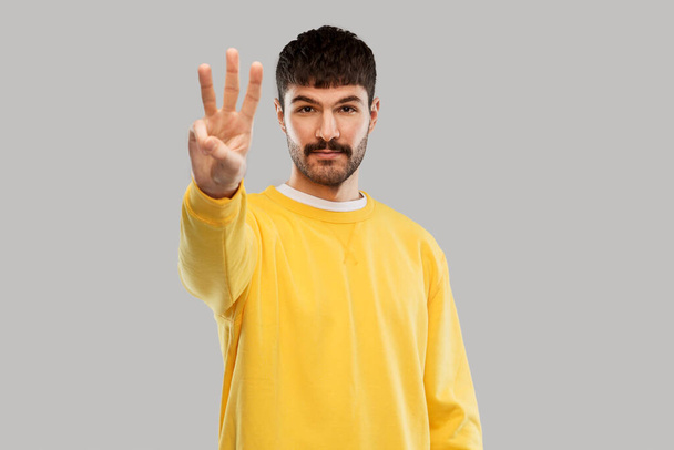 man in yellow sweatshirt showing three fingers - Fotoğraf, Görsel
