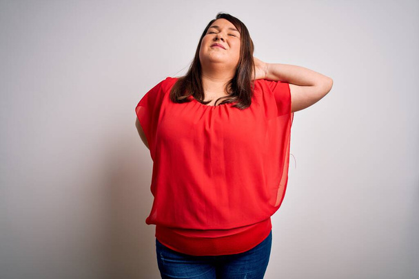 Beautiful brunette plus size woman wearing casual red t-shirt over isolated white background Suffering of neck ache injury, touching neck with hand, muscular pain - Valokuva, kuva