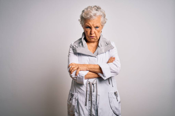 Senior mooie grijs-harige vrouw draagt casual jas staan over witte achtergrond sceptisch en nerveus, afkeurende uitdrukking op gezicht met gekruiste armen. Negatief persoon. - Foto, afbeelding