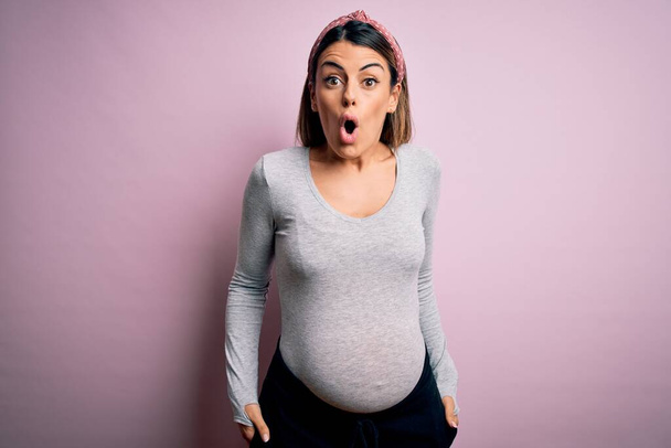 Mladá krásná brunetka žena těhotná čeká dítě přes izolované růžové pozadí strach a šokován překvapením výraz, strach a vzrušený obličej. - Fotografie, Obrázek