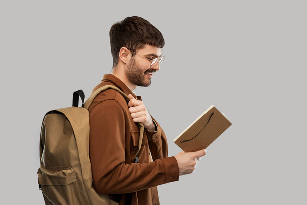 smiling young man with backpack reading diary - Foto, Imagen