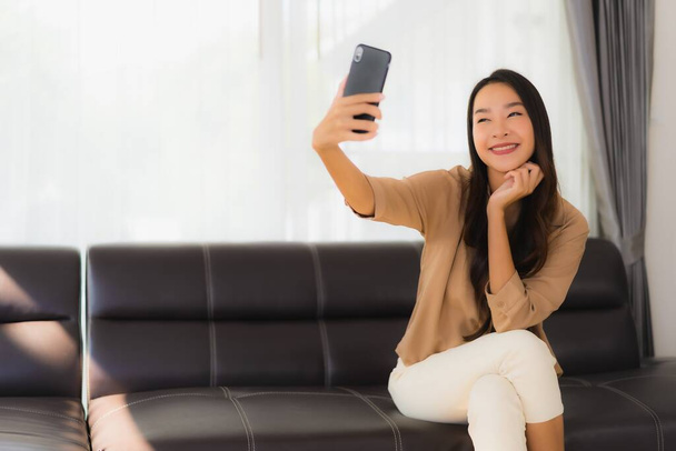 Ritratto bella giovane donna asiatica utilizzare smartphone cellulare o cellulare con tazza di caffè sul divano soggiorno interno
 - Foto, immagini