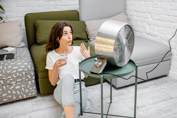 vrouw koelt zichzelf met een ventilator thuis - Foto, afbeelding