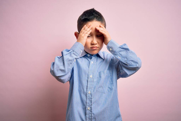 Jeune garçon enfant portant chemise élégante debout sur fond rose isolé souffrant de maux de tête désespérés et stressés parce que la douleur et la migraine. Mains sur la tête
. - Photo, image