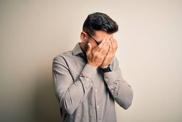 Young handsome man wearing elegant shirt and glasses over isolated white background with sad expression covering face with hands while crying. Depression concept. - Photo, Image
