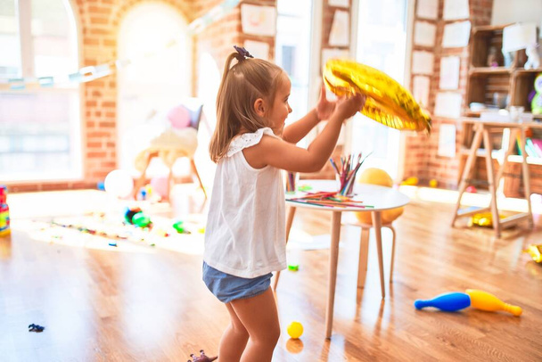 Молодая красивая блондинка девочка наслаждается игрой школы с игрушками в детском саду, улыбаясь счастливо играть с воздушным шаром дома
 - Фото, изображение