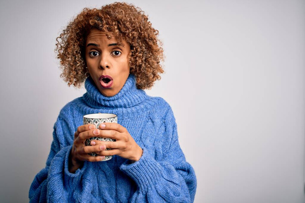 Young african american curly woman drinking mug of coffee over isolated white background scared in shock with a surprise face, afraid and excited with fear expression - Zdjęcie, obraz