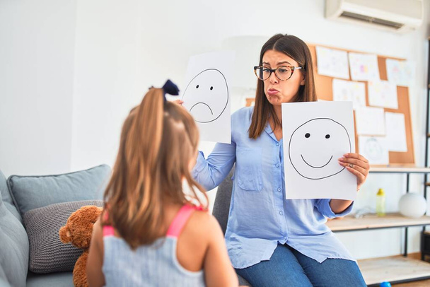 Young therapist woman speaking and treating child, counselor and behaviour correction at pedagogue payroom showing happy and sad faces - Foto, afbeelding