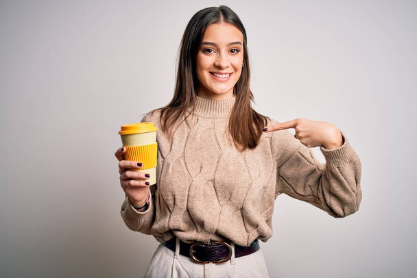 Giovane bella donna bruna bere un bicchiere di caffè su sfondo bianco isolato con faccia a sorpresa puntando il dito verso se stesso
 - Foto, immagini